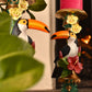 Decorative figurines of toucans with floral elements on a candle holder.