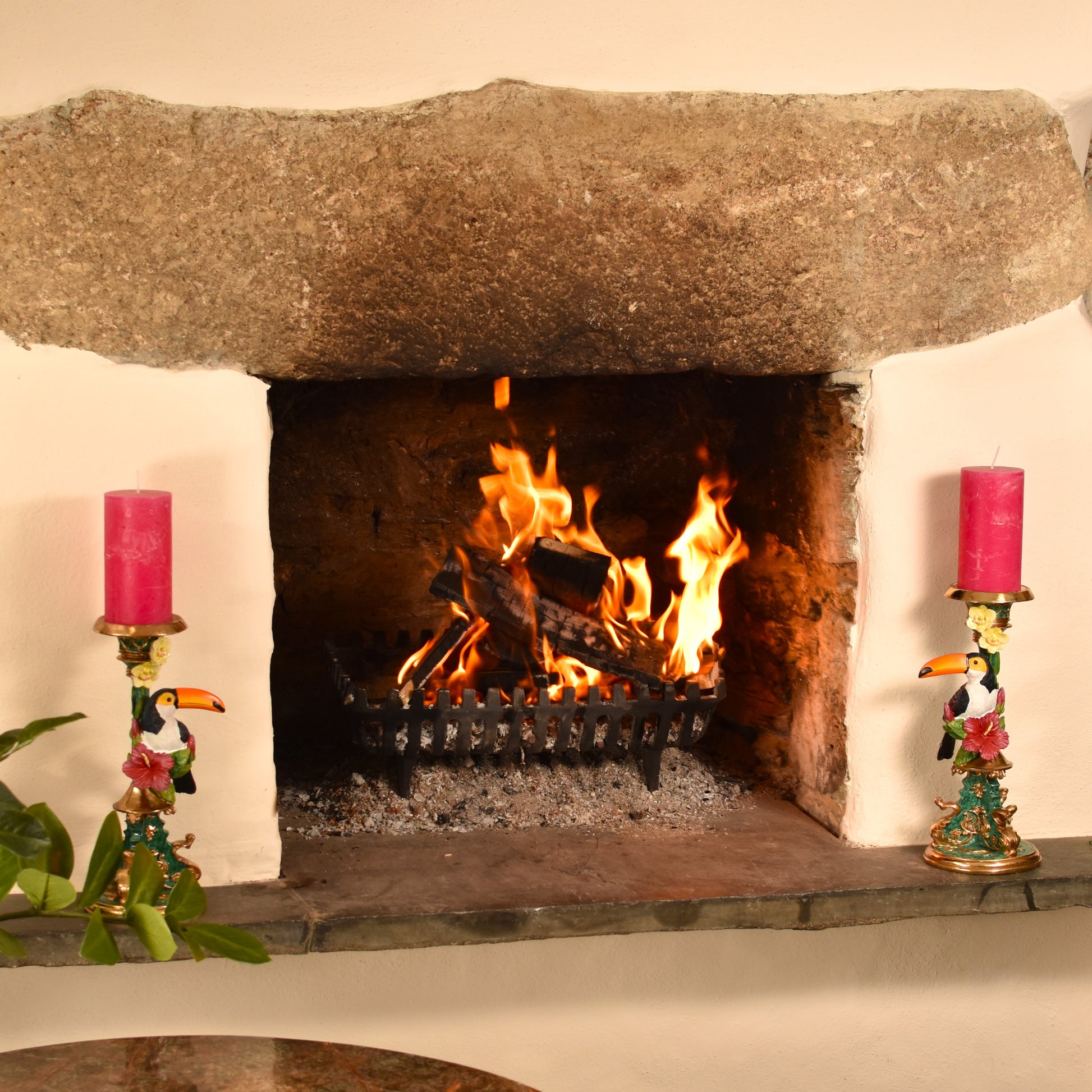 Fireplace with burning logs, flanked by decorative toucan candle holders with pink candles.